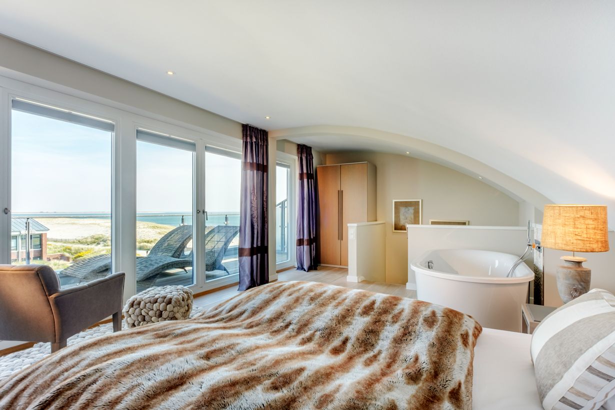 Doppelbett, Balkon mit Liegen und freistehender Badewanne in der Mastersuite vom Hotel Strand